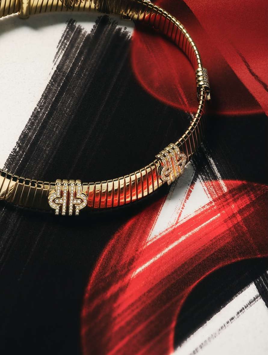 Close-up of a gold, articulated necklace with jewel embellishments on a white and red painted backdrop. Jewellery is the primary focus.