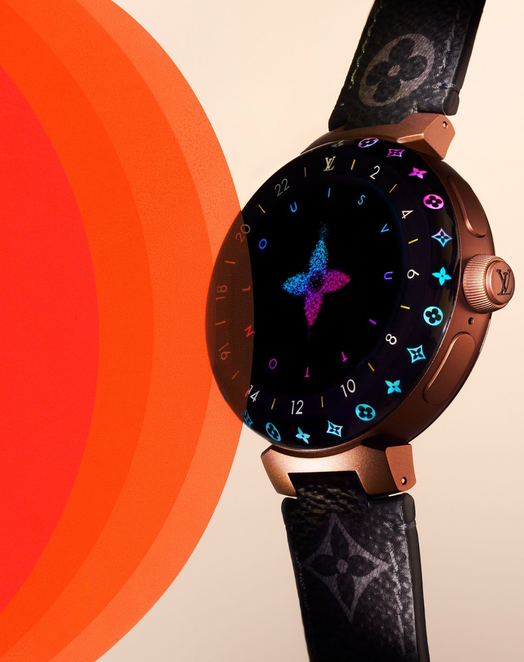 Close-up studio shot of a smart watch with a dark face, rose gold casing, and monogrammed leather strap on an off-white background.