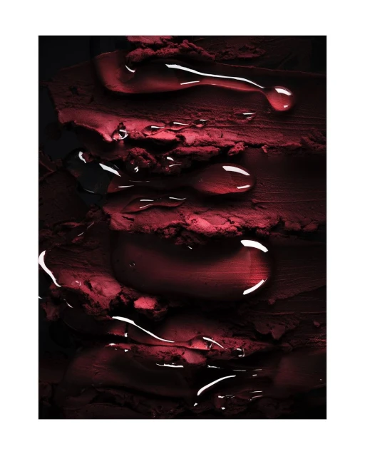 Macro image of dark red lipstick smears with clear water droplets, creating a textured, glossy beauty product aesthetic.