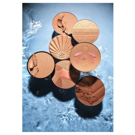 Overhead shot of bronze makeup compacts in a water basin. Compacts display seashell, botanical, and geometric designs in the powder.