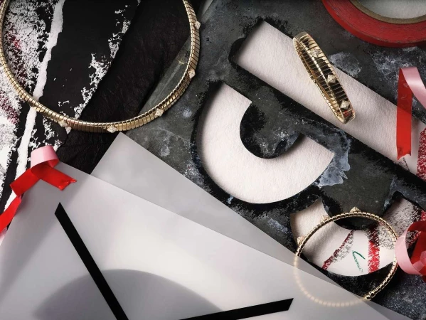 Close-up still life photography featuring gold diamond jewelry arranged across textured dark surfaces and translucent paper layers.