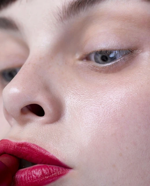 Close-up portrait of a young adult woman with red lipstick, focusing on her facial features and makeup in a beauty context.