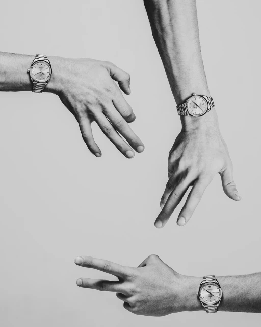 Three male hands in a studio setting each wearing a wristwatch, one hand making a peace sign against a grey monochromatic background.
