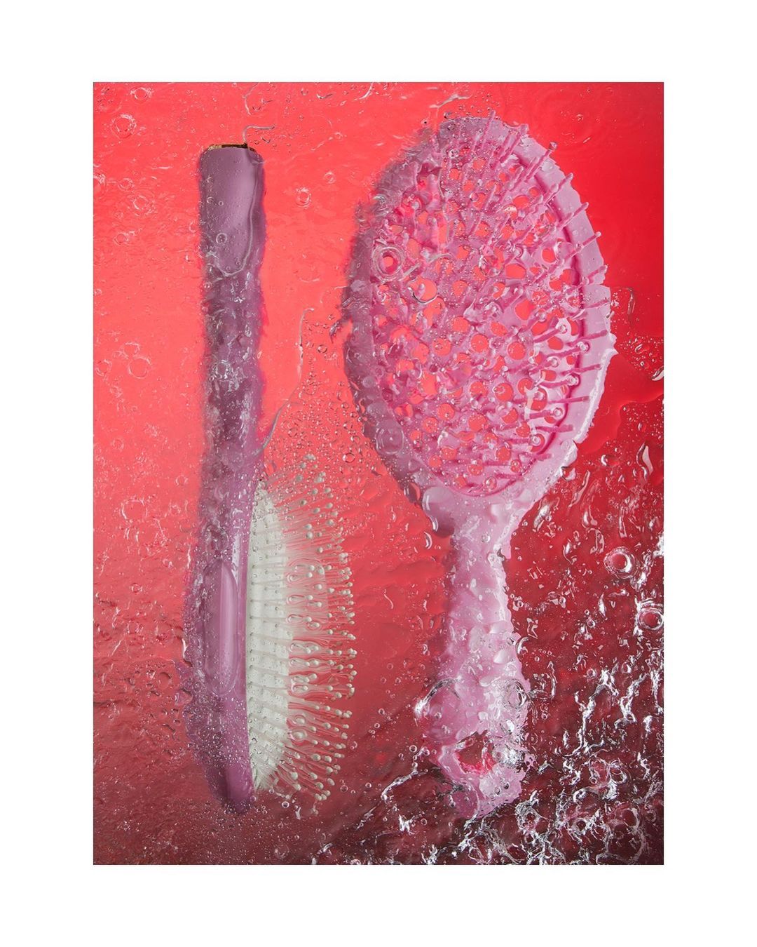 Two pink hairbrushes are photographed under water against a red backdrop, creating a visually striking image with unique lighting effects.