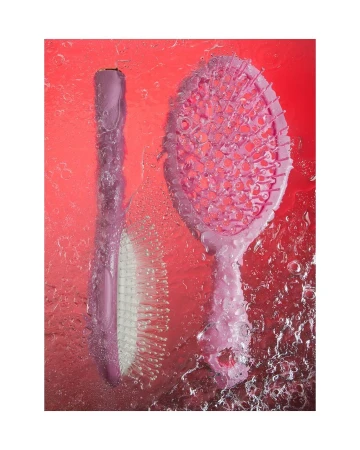 Two pink hairbrushes are photographed under water against a red backdrop, creating a visually striking image with unique lighting effects.