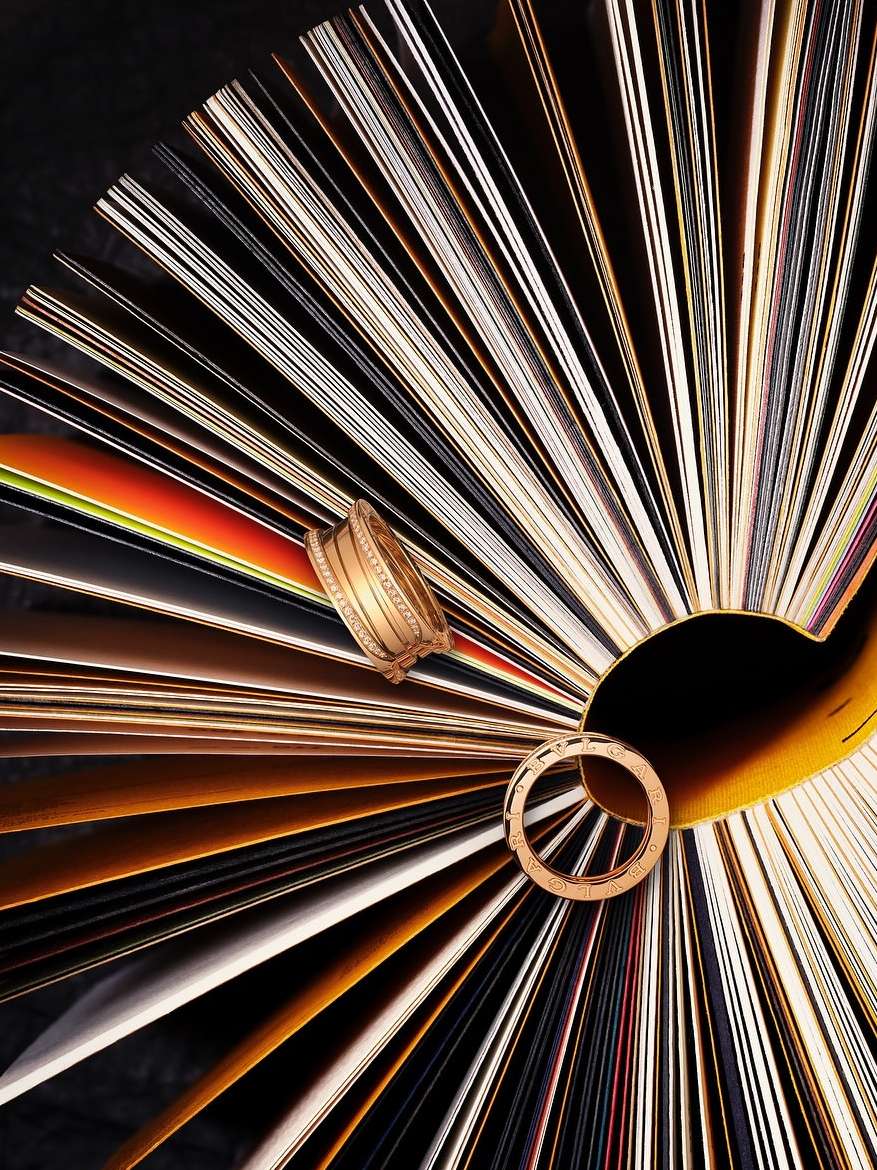 Overhead shot of gold bracelets and ring arranged on a textured fan-like backdrop of multi-colored paper for a visually striking composition.