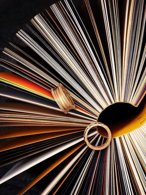 Overhead shot of gold bracelets and ring arranged on a textured fan-like backdrop of multi-colored paper for a visually striking composition.