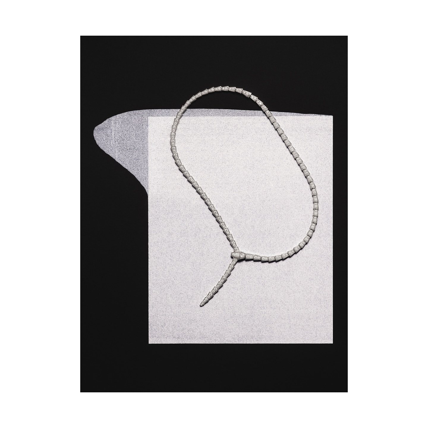 Elegant necklace made of white beads knotted on a textured paper background, against a solid black backdrop, jewelry product shot.