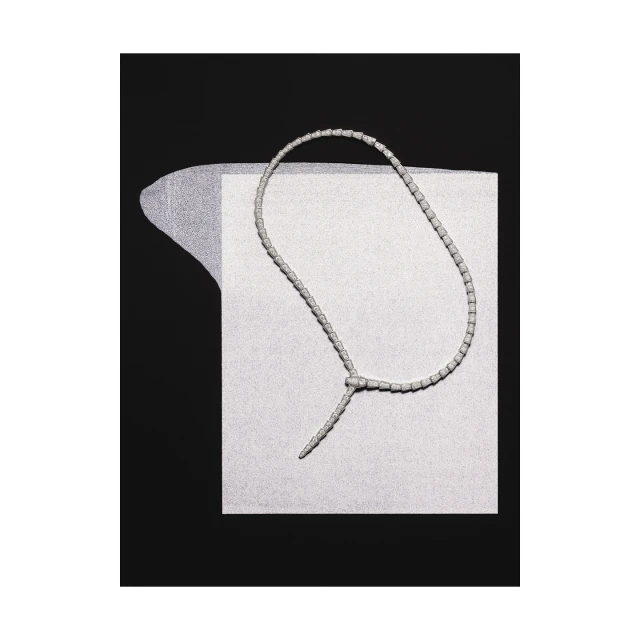Elegant necklace made of white beads knotted on a textured paper background, against a solid black backdrop, jewelry product shot.