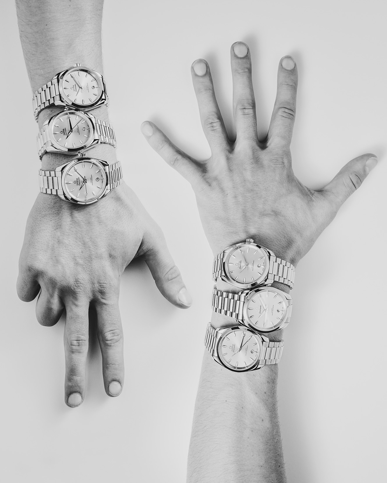 Close-up studio shot of two hands adorned with multiple silver wristwatches on a white background, showcasing a unique and eye-catching display.
