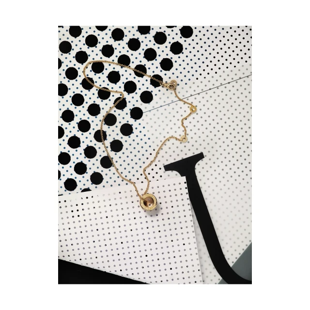 Gold necklace with circle pendant on a white and black polka dot background. Jewelry product shot in a simple, elegant studio setting.