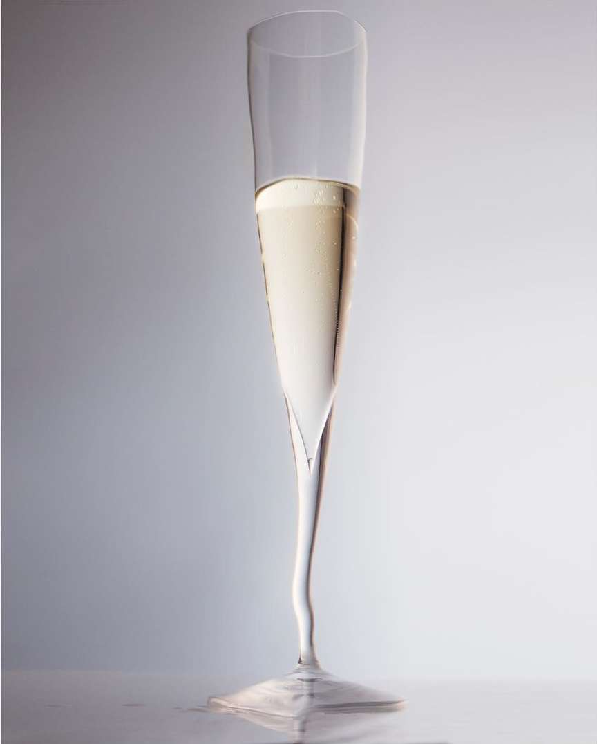 Elegant champagne flute filled with bubbly drink on light background. Tall glass with a unique curved stem and a clear liquid inside.