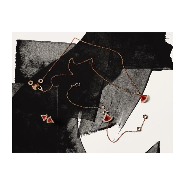 High-angle studio shot of a rose gold necklace, a bracelet, and earrings against a black and white abstract painted background.