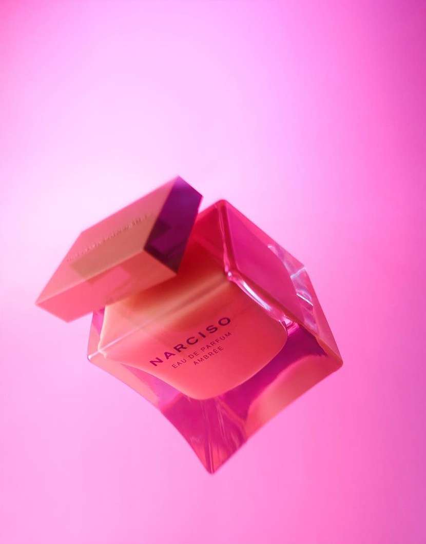 A pink perfume bottle angled diagonally with its cap slightly detached against a solid pink background.