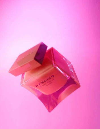 A pink perfume bottle angled diagonally with its cap slightly detached against a solid pink background.