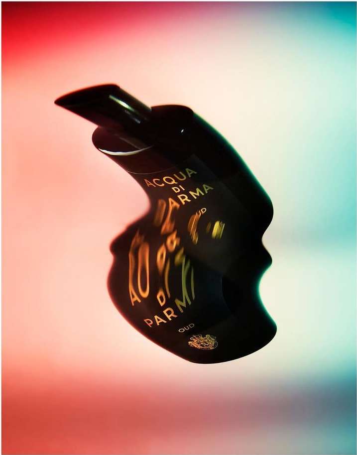Acqua di Parma Oud perfume bottle. Dark brown glossy material. Red and blue gradient background. Luxurious beauty product.