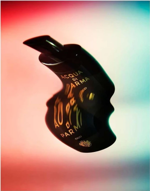 Acqua di Parma Oud perfume bottle. Dark brown glossy material. Red and blue gradient background. Luxurious beauty product.