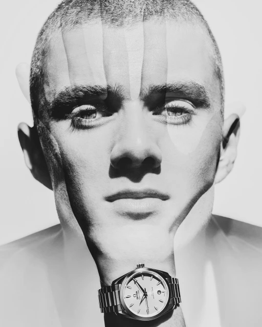Monochrome portrait of a young adult male with a close buzzcut hairstyle and a wristwatch, overlaid with transparent hand silhouette.