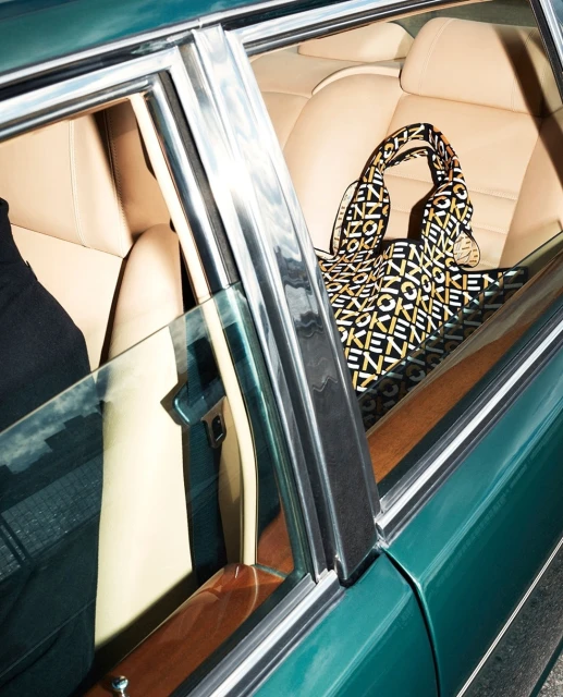 Interior view of a teal vintage car showcasing tan leather seats and a designer handbag with a geometric logo pattern.