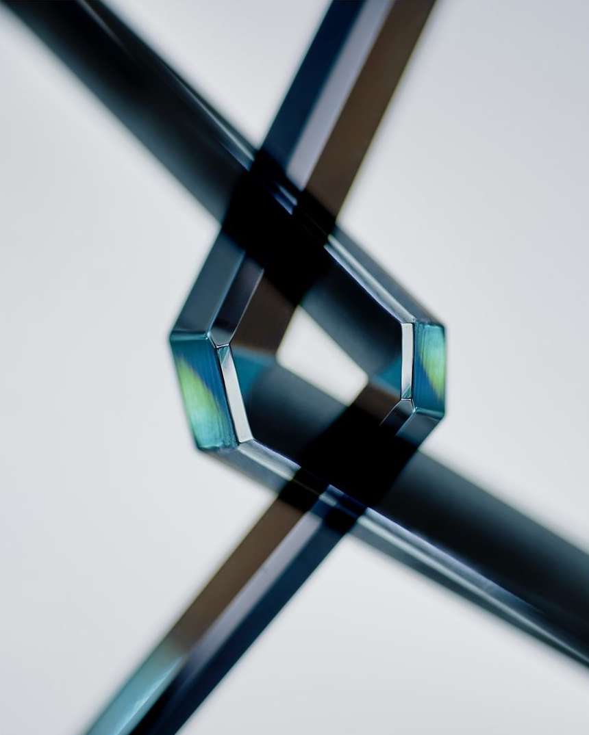 Abstract image of intersecting translucent tubes creating geometric shapes and sharp shadows against a plain light backdrop. 