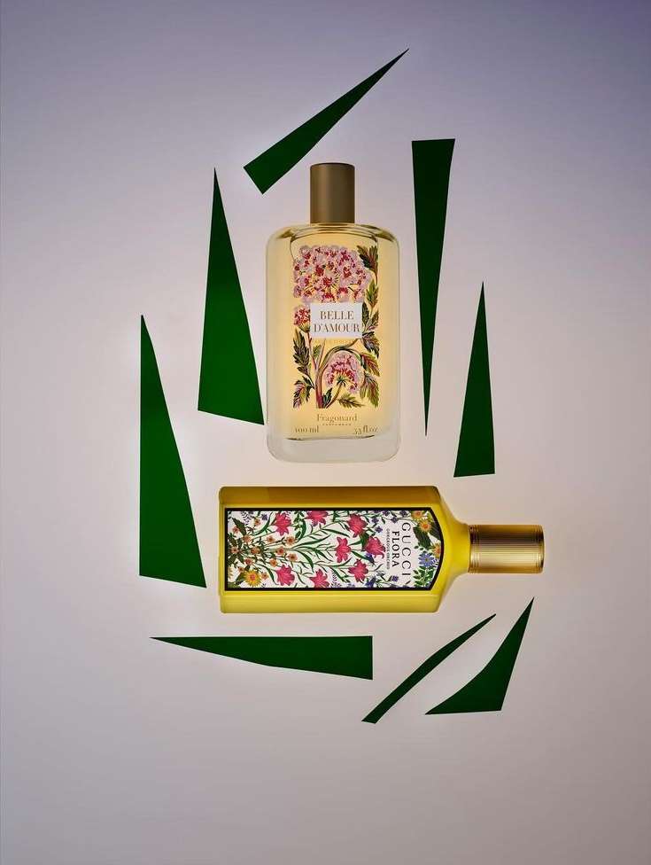 Two Gucci Flora perfumes, one rectangular and one cylindrical, presented on a pale background with geometric green paper shapes.