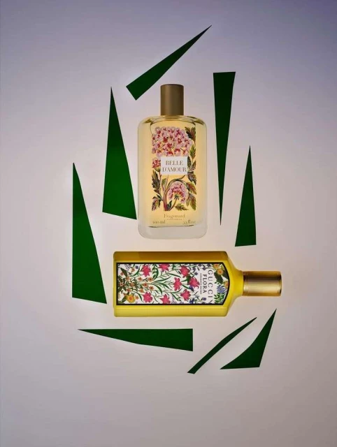 Two Gucci Flora perfumes, one rectangular and one cylindrical, presented on a pale background with geometric green paper shapes.