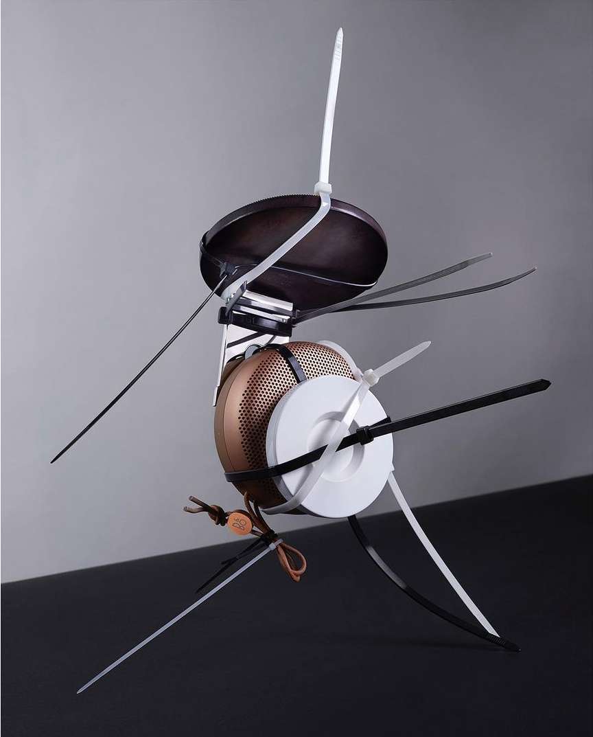 Abstract sculpture made of kitchen utensils and zip ties against a grey background. Dominant colors are white, black, brown and grey.