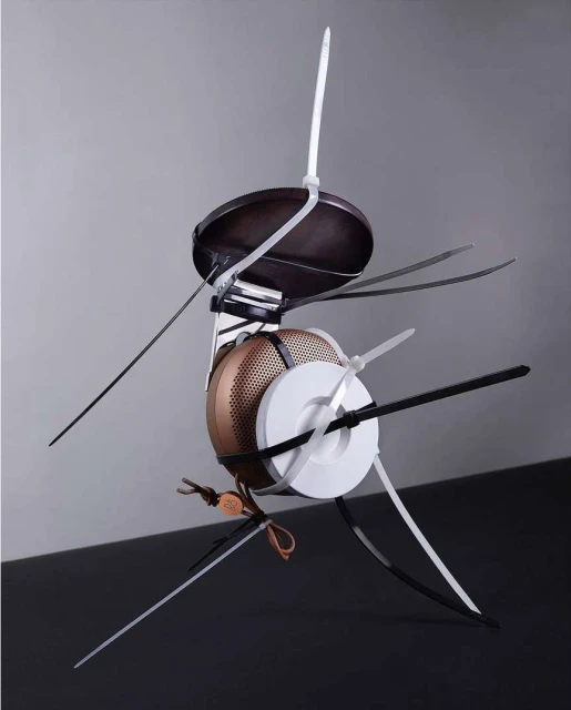 Abstract sculpture made of kitchen utensils and zip ties against a grey background. Dominant colors are white, black, brown and grey.