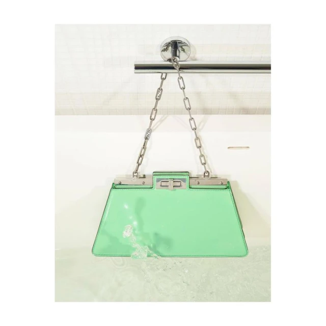 A turquoise patent leather Fendi bag with silver hardware hangs over a bathtub filled with water for a high fashion product shot.