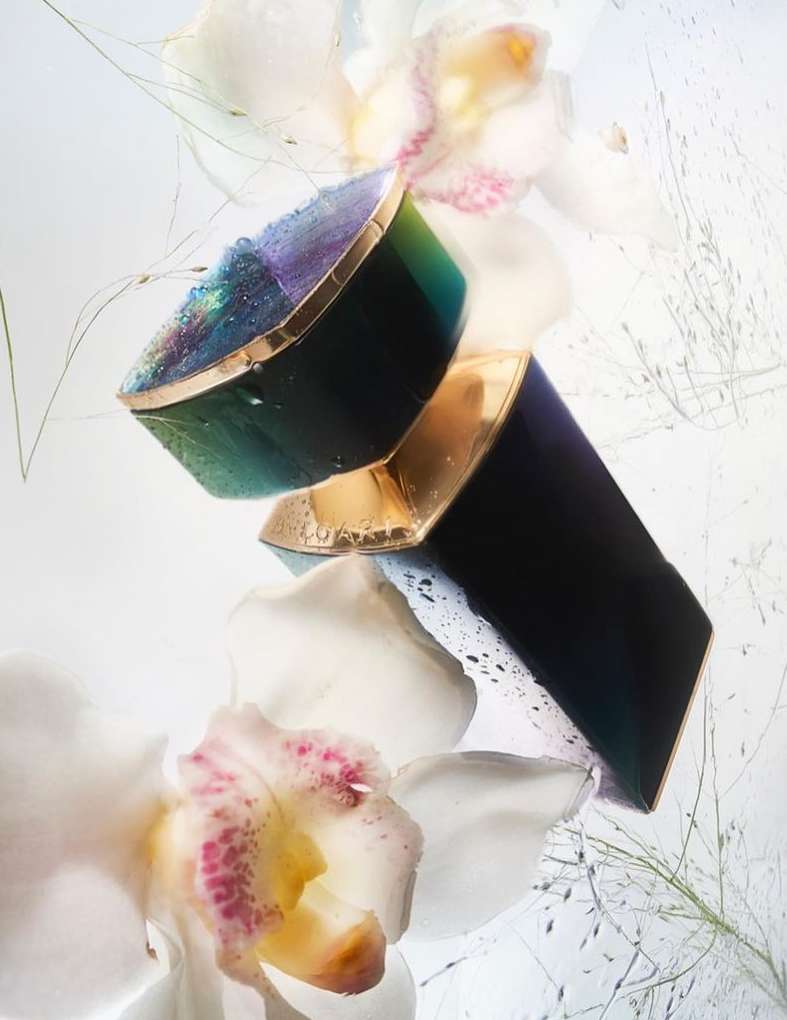 Cosmetic product featuring a dark, geometric container, set among delicate white orchids and fine, airy grasses, with a clean, bright background.