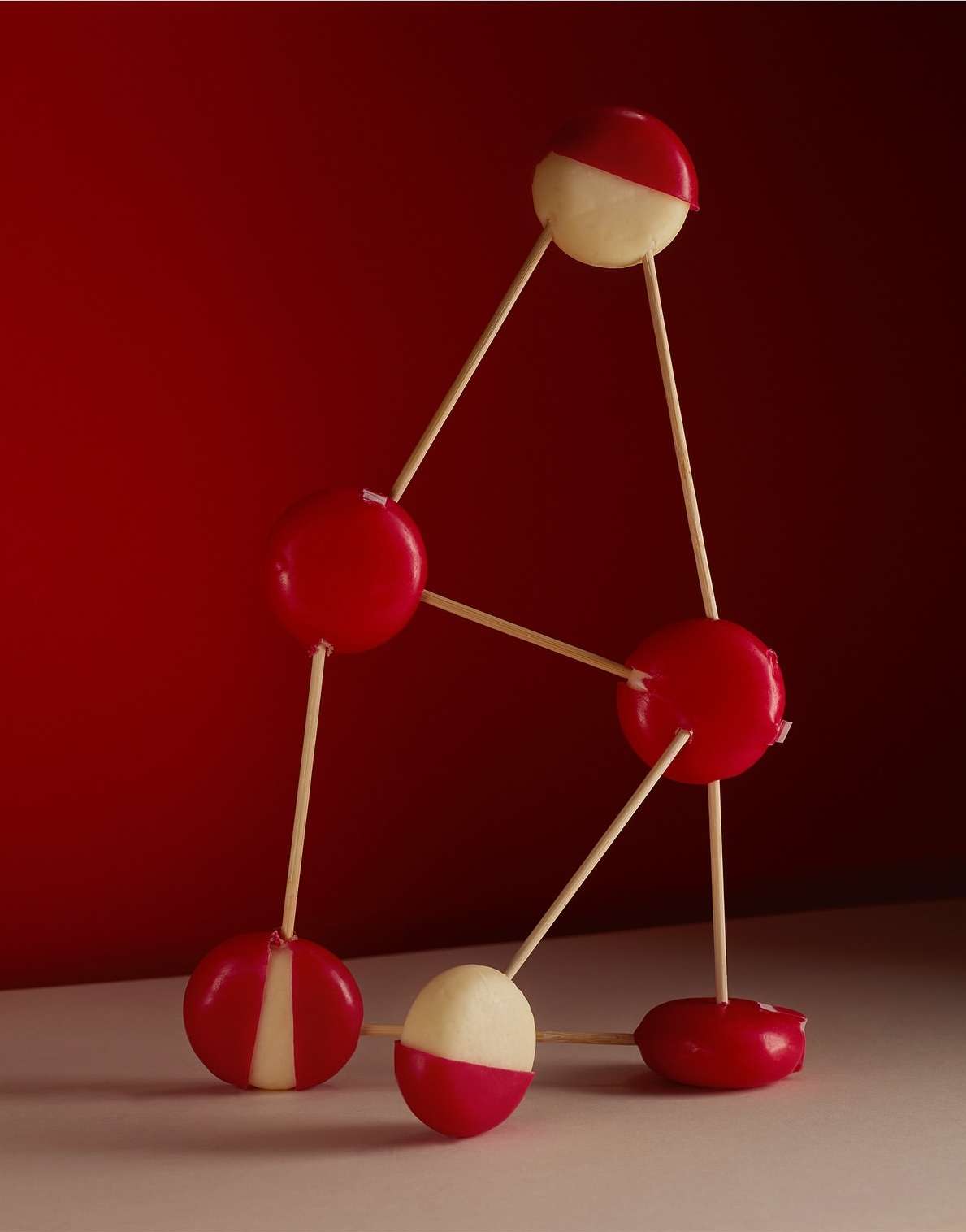 Artistic shot of red and white cheese balls connected by wooden sticks against a red background. Still life studio shot of food.