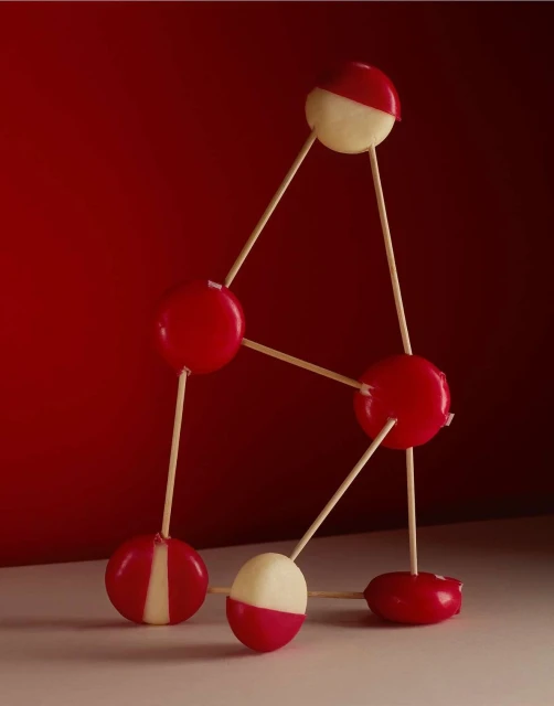 Artistic shot of red and white cheese balls connected by wooden sticks against a red background. Still life studio shot of food.