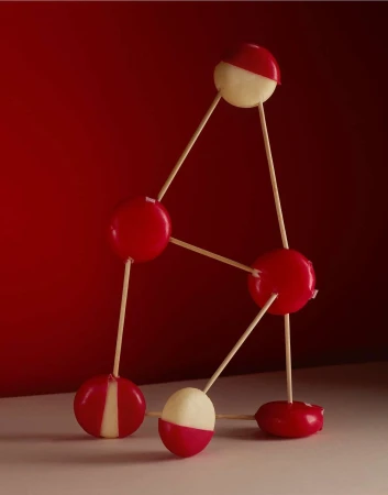 Artistic shot of red and white cheese balls connected by wooden sticks against a red background. Still life studio shot of food.