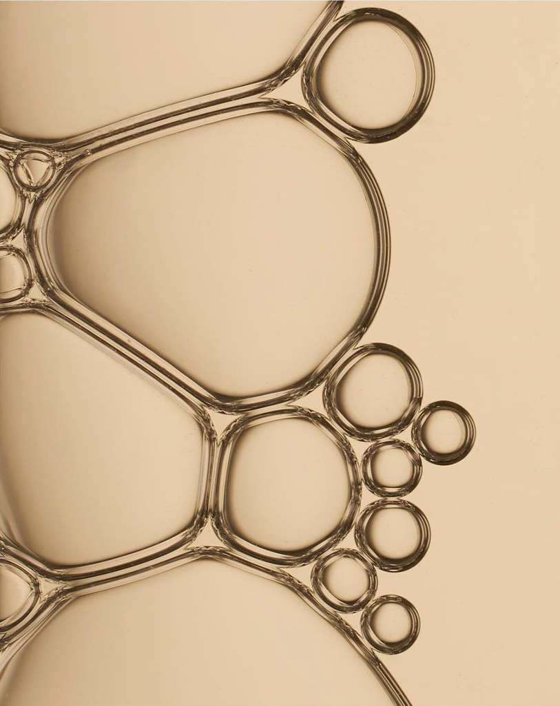 Macro photograph of connected translucent bubbles against a neutral backdrop, showcasing abstract patterns and refractions.