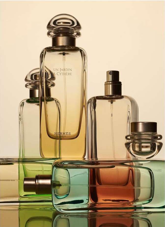 Still life of multiple glass perfume bottles with gold caps and colorful gradient perfume on a reflective surface against a gradient background.