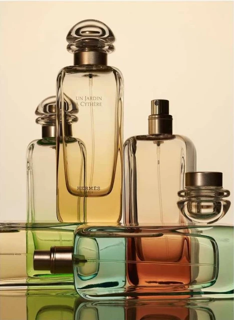 Still life of multiple glass perfume bottles with gold caps and colorful gradient perfume on a reflective surface against a gradient background.