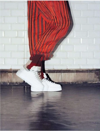 Close-up of red and black striped trousers paired with white platform sneakers against white tiled wall