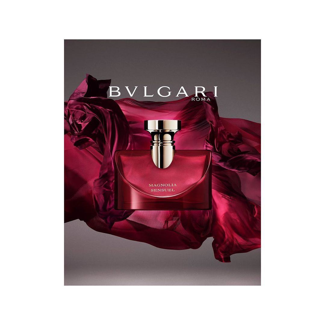 Elegant still life of Bulgari's 'Magnolia Sensuel' perfume bottle against a draped burgundy fabric, capturing luxury and sophistication.