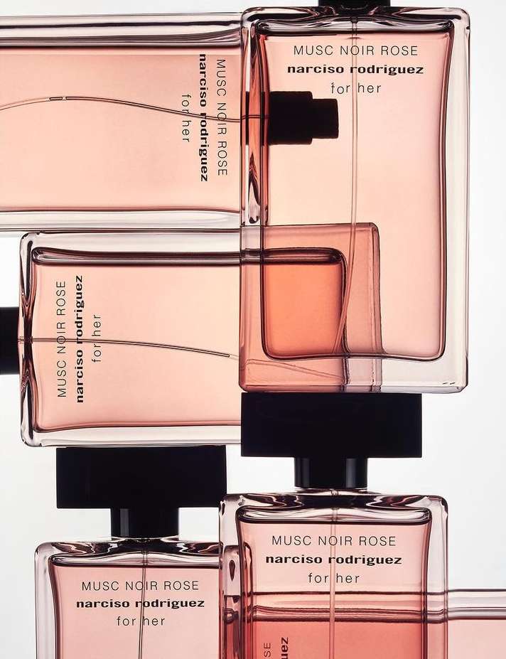 Stacked clear glass perfume bottles filled with pink liquid, featuring black nozzle caps and brand labeling against a bright white backdrop.