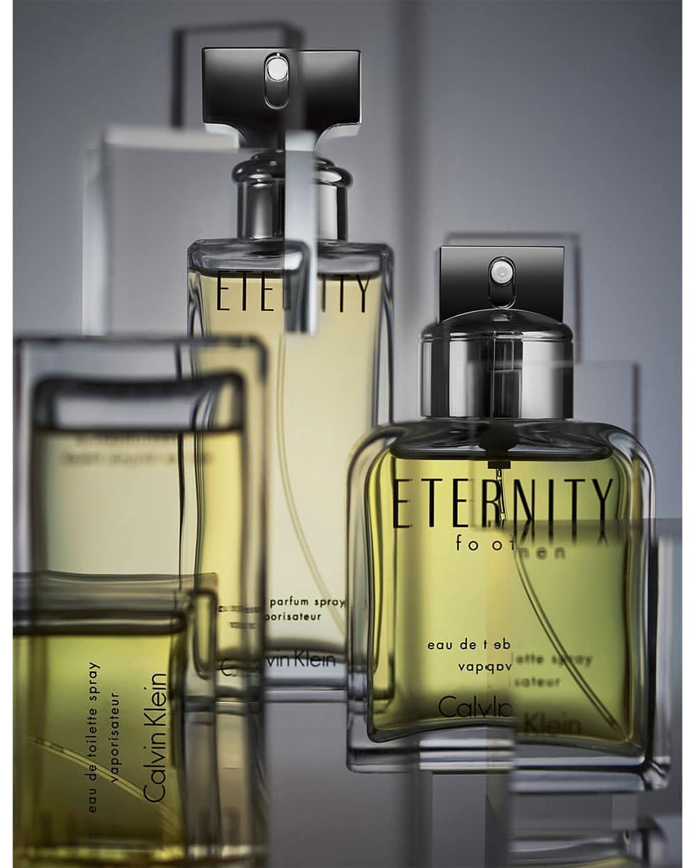 Close-up studio shot of Calvin Klein Eternity for Men fragrance bottles with black caps, on a reflective surface and blurred background.