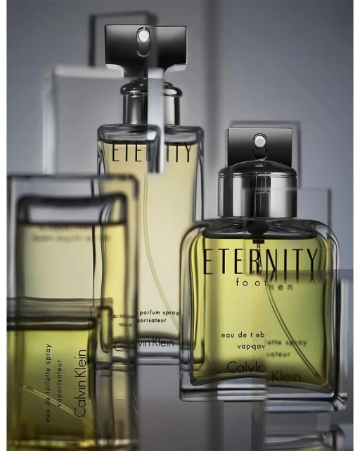 Close-up studio shot of Calvin Klein Eternity for Men fragrance bottles with black caps, on a reflective surface and blurred background.