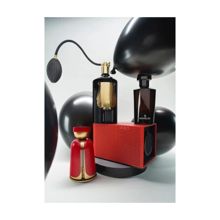 Still life studio shot features two perfume bottles, a speaker, and decorative figure against a gradient white backdrop, accentuated by black balloons.