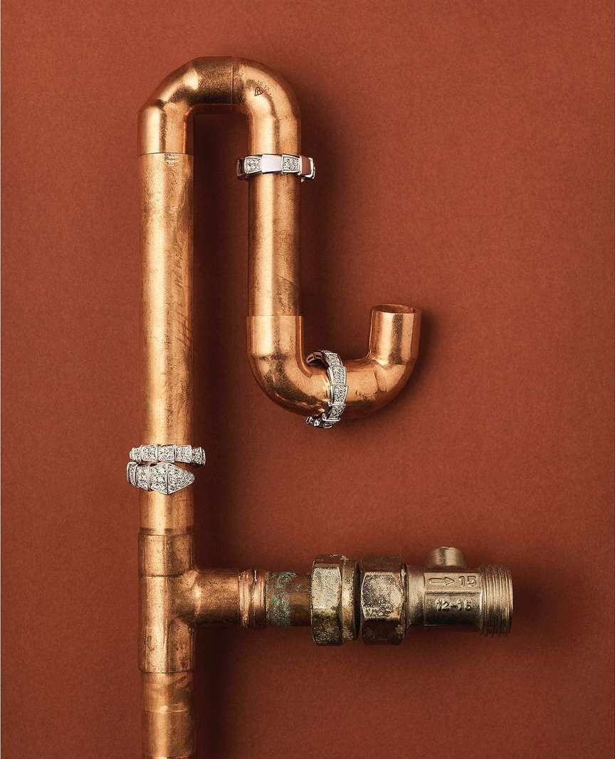 Still life shot of copper pipes connected in a geometric design, adorned with white metal rings on a brown background.