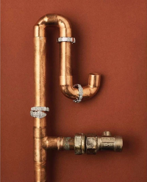 Still life shot of copper pipes connected in a geometric design, adorned with white metal rings on a brown background.