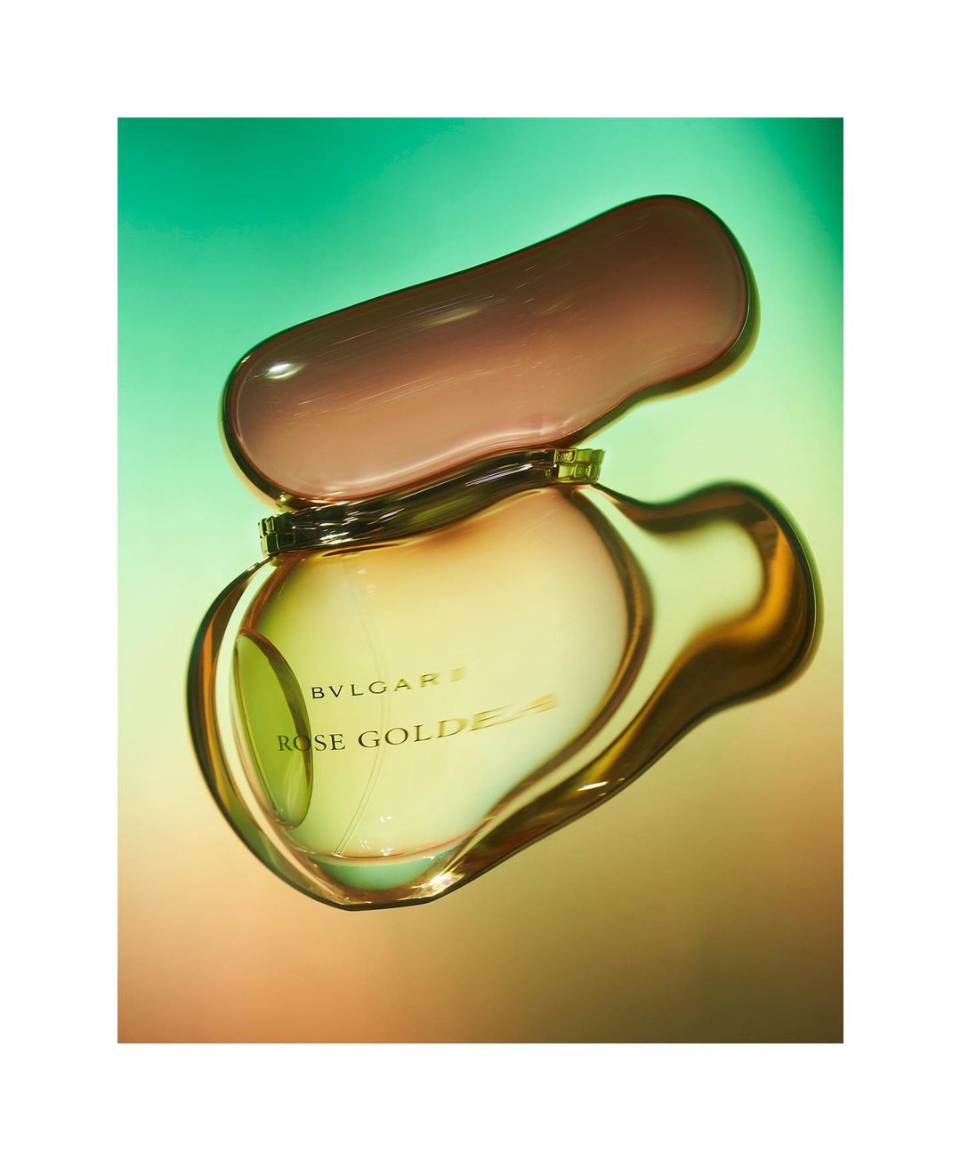 Still life studio shot of an open Bvlgari Rose Goldea perfume bottle on a gradient green and orange background with soft lighting.