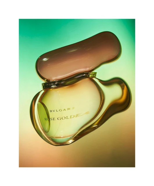 Still life studio shot of an open Bvlgari Rose Goldea perfume bottle on a gradient green and orange background with soft lighting.