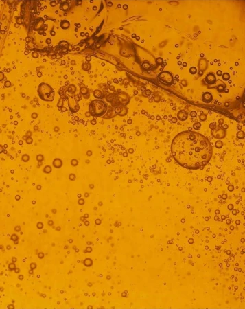 Abstract close-up of amber liquid with bubbles, creating a textured and visually interesting surface. Ideal for backgrounds or textures.