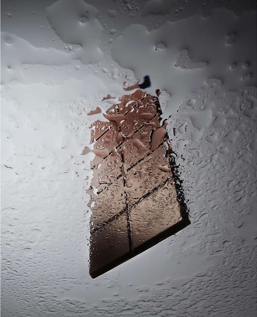 Close-up shot of a chocolate bar against a wet glass backdrop with water droplets, creating an abstract and textured food scene.