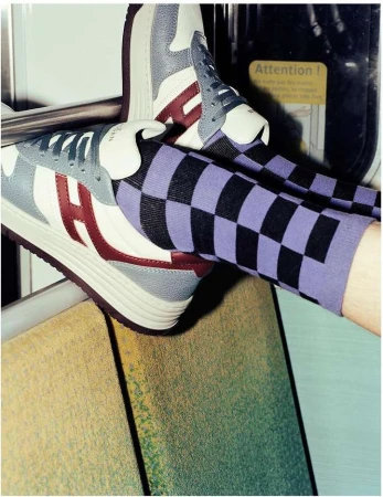 Close-up of feet wearing purple and black checkered socks and leather sneakers inside a public transport vehicle