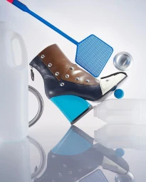 A multi-panel designer ankle boot surrounded by household plastic objects and a blue flyswatter on a white background